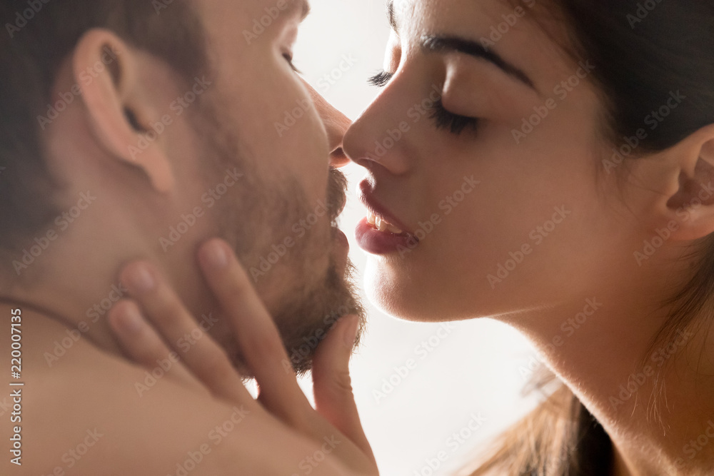 Close up of sensual young couple facing each other close to kiss, girlfriend touching boyfriend chin enjoying intimate moment together, romantic lovers with eyes closed having tender love foreplay Close up of sensual young couple facing each other close to kiss, girlfriend touching boyfriend chin enjoying intimate moment together, romantic lovers with eyes closed having tender love foreplay