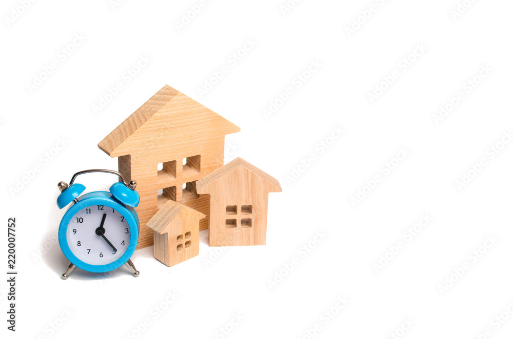 Wooden houses and a blue alarm clock on a white background. The concept of rent housing monthly and hourly. Temporary affordable accommodation, hotels and hostels. Return On Investment