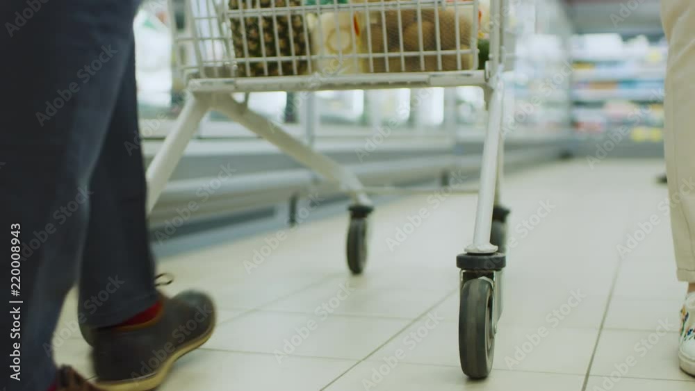 Following Low Ground Shot At the Supermarket: of the Legs and Shopping Cart Full of Products Moving Through Frozen Goods Section of the Store. Following Low Ground Shot At the Supermarket: of the Legs and Shopping Cart Full of Products Moving Through Frozen Goods Section of the Store.