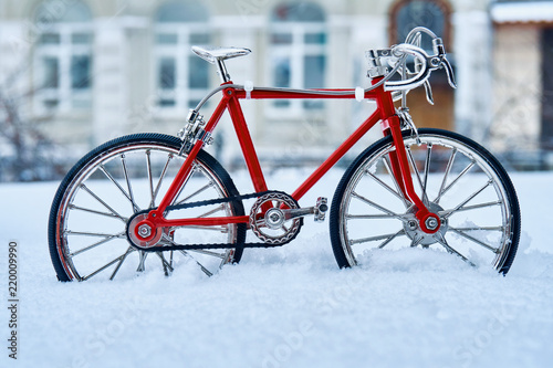 A toy model of a red bicycle made of metal, executed with good accuracy, is in winter in snowdrifts and cold weather on a city street