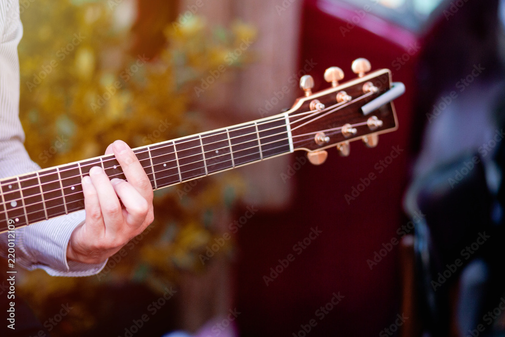 Fototapeta premium Guitar with a man's male hands playing the guitar on wooden wall background, electric or acoustic guitar with nature light. Concept of guys boys band performing on events 