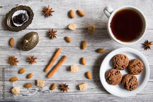 Chocolate cookies with black tea, nuts, almonds, anise stars, brown sugar, dates and cinnamon sticks on wooden background, top view, Christmas concept.