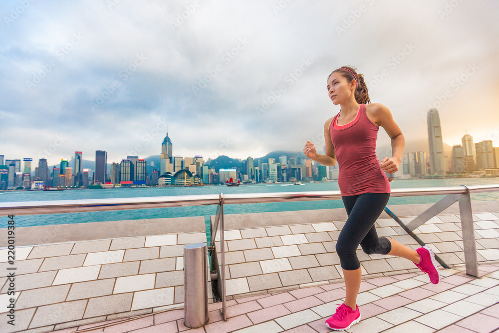 Running woman girl runner at Hong Kong skyline city background. Asian athlete jogging training living healthy lifestyle on Tsim Sha Tsui  Avenue of Stars in Victoria Harbour, Kowloon.