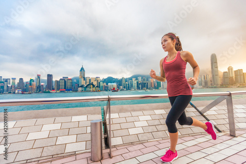 Running woman girl runner at Hong Kong skyline city background. Asian athlete jogging training living healthy lifestyle on Tsim Sha Tsui Avenue of Stars in Victoria Harbour, Kowloon.