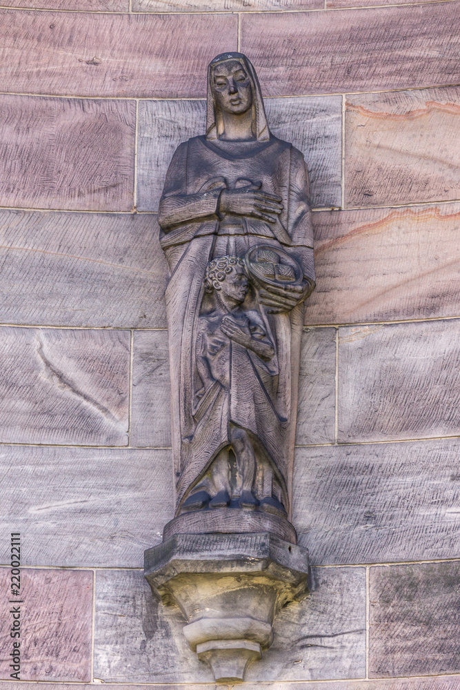Φωτογραφία Edinburgh, Scotland, UK - June 14, 2012: Stone Mother and child statue set against beige brown wall with her holding basket of bread