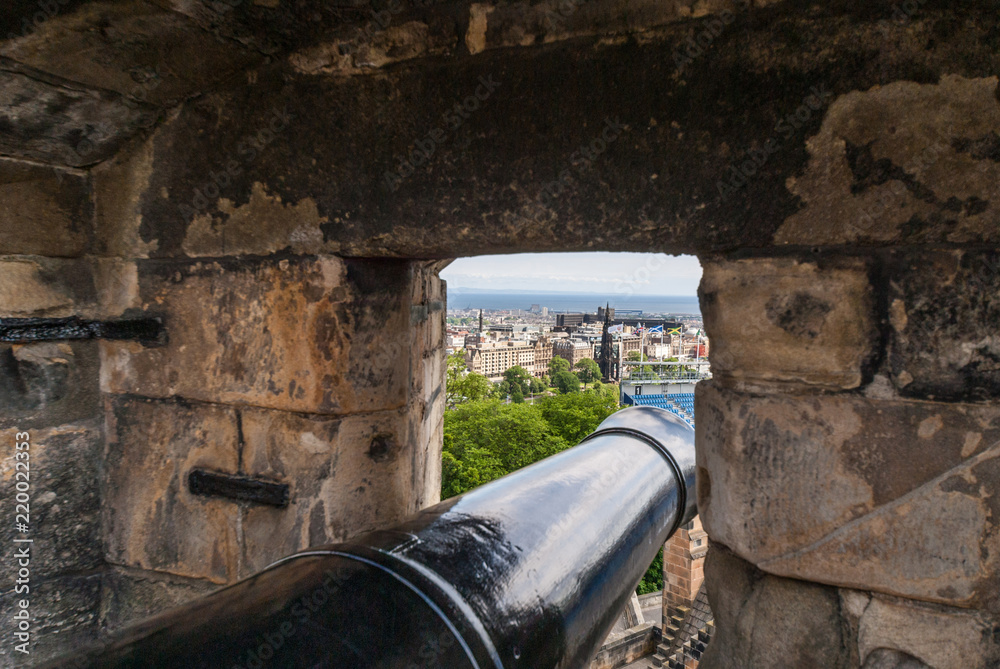 Φωτογραφία Edinburgh, Scotland, UK - June 14, 2012: Looking along barrel of black cannon set in niche over the city behind gray stone rampart