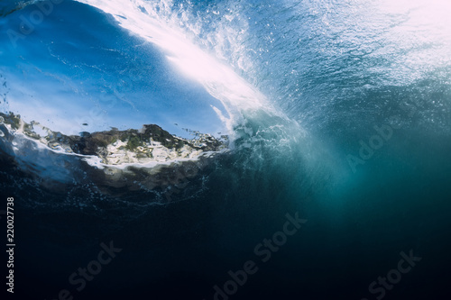 Barrel wave crashing in tropical ocean with sunlight. Underwater view