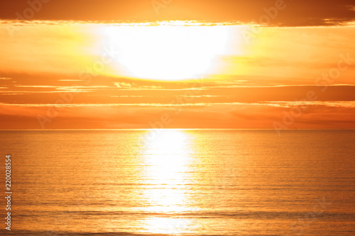 Bright golden dramatic sunset sun reflecting orange  gold  off calm ocean