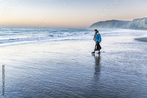 Beautiful young girl walking with it wet ankles along the sea water on an amazing wild beach during a sunny day at sunset time in Topocalma Beach, Puertecillo, Chile