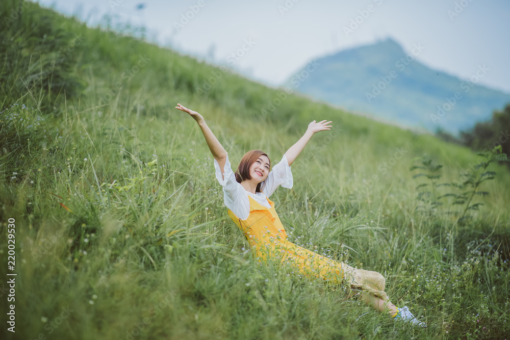 Beautiful Asian young woman shot hair wearing yellow dress  joyful, smiling with arms raised up over mountain background.  Thai happy woman at  Bang Pra Dam Chonburi Thailand.