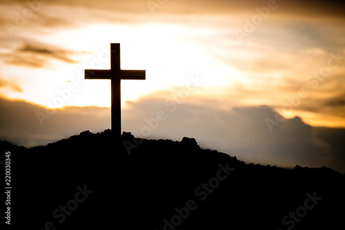 The silhouette cross standing on meadow sunset and flare background.Cross on a hill as the morning sun comes up for the day.The cross symbol for Jesus christ. Christianity, religious, faith, Jesus .