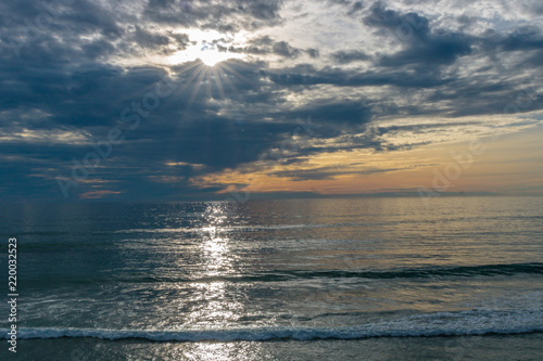 Sunset seascape  orange  blue  yellow sky  with aqua marine green sea  white waves rolling in  pacific ocean  background photo of sun setting