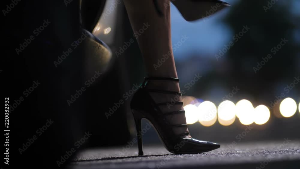 Car's door opens, woman's legs in sexy high heels stiletto shoes stepping out of automobile in night city and walking to camera. Female in high heels getting out of car on bokeh lights background