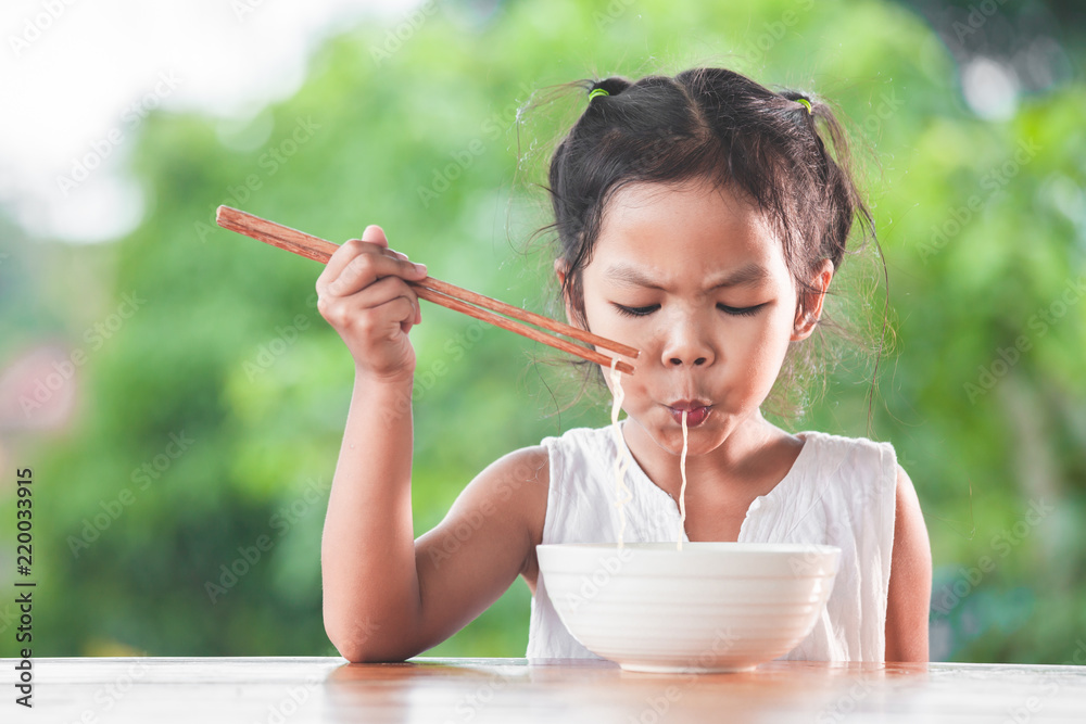 Cute asian child girl eating delicious instant noodles with chopstick in the nature background Cute asian child girl eating delicious instant noodles with chopstick in the nature background