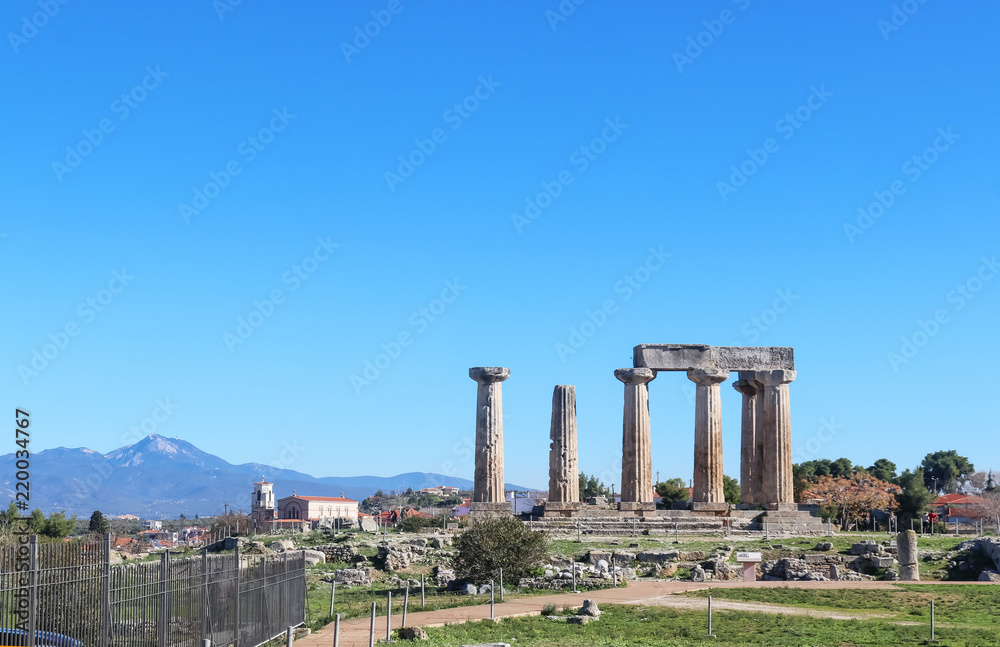 The ruins of the Temple of Apollo at ancient Corith Greece with a church and village and high mountains in the background