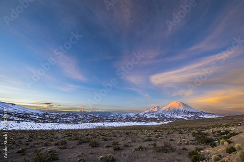 The great "Nevados de Payachatas" with the Pomerape and Parinacota Volcanoes, left and right respectively over the Atacama desert meadows during sunset an amazing colorful landscape, Arica, Chile