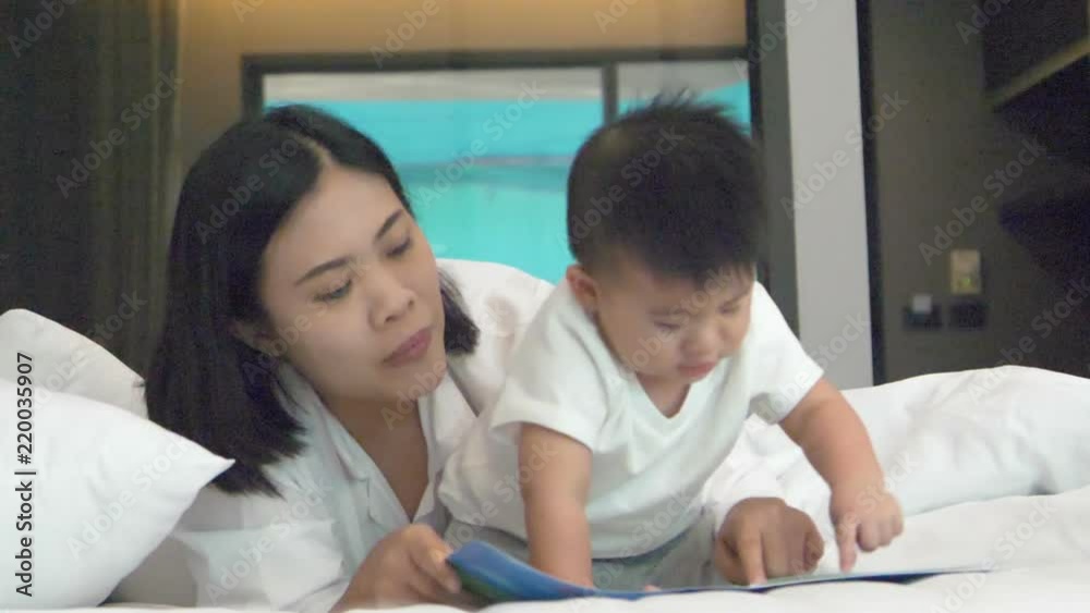 Mother actually enjoy reading a book with baby boy on the bed at home