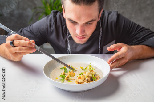 Cook chef making creme soup with herbs, mushrooms, scallops and toast bred.