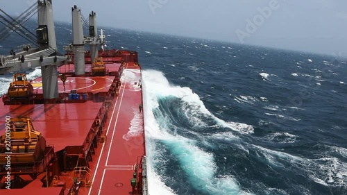 Cargo ship rolling in stormy sea. Huge waves under blue sky in Indian Ocean