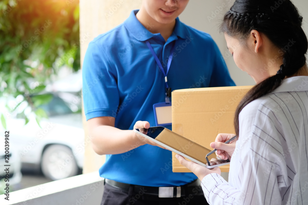 Woman appending signature sign on tablet after accepting receive boxes from delivery man, woman sign on digital tablet, receive delivery concept Woman appending signature sign on tablet after accepting receive boxes from delivery man, woman sign on digital tablet, receive delivery concept