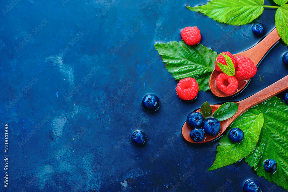 Summer berries in wooden spoons top view. Raspberry and blueberry mix on a dark blue wet background with copy space. Raw ingredients from above