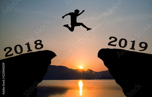 A young man jump between 2018 and 2019 years over the sun and through on the gap of hill silhouette evening colorful sky. happy new year 2019.