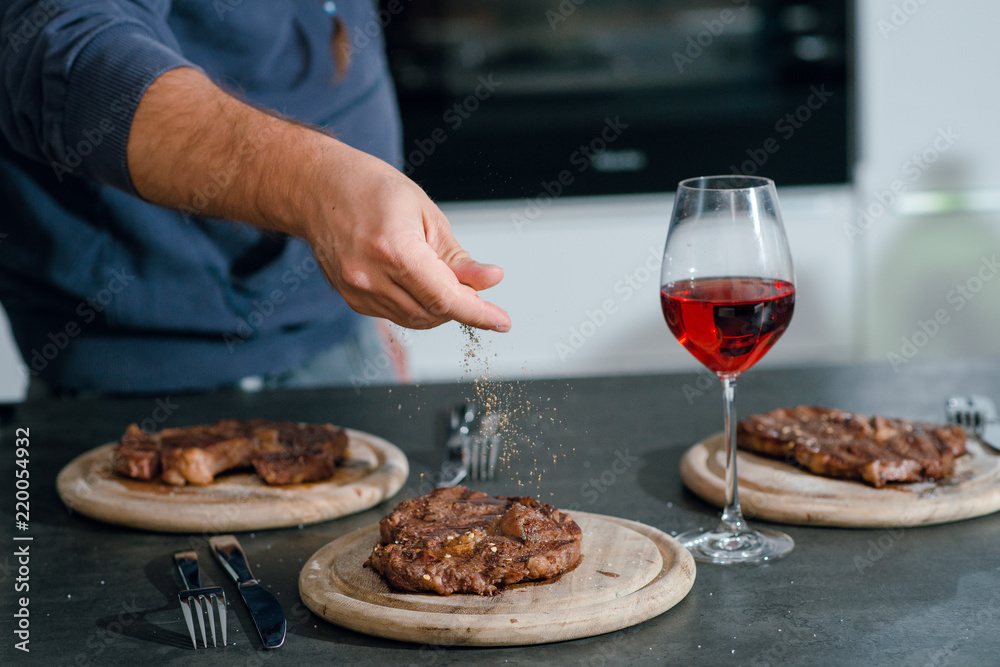 Man putting herbs and spices on the grilled well done steaks. Dinner with red wine. Man putting herbs and spices on the grilled well done steaks. Dinner with red wine.