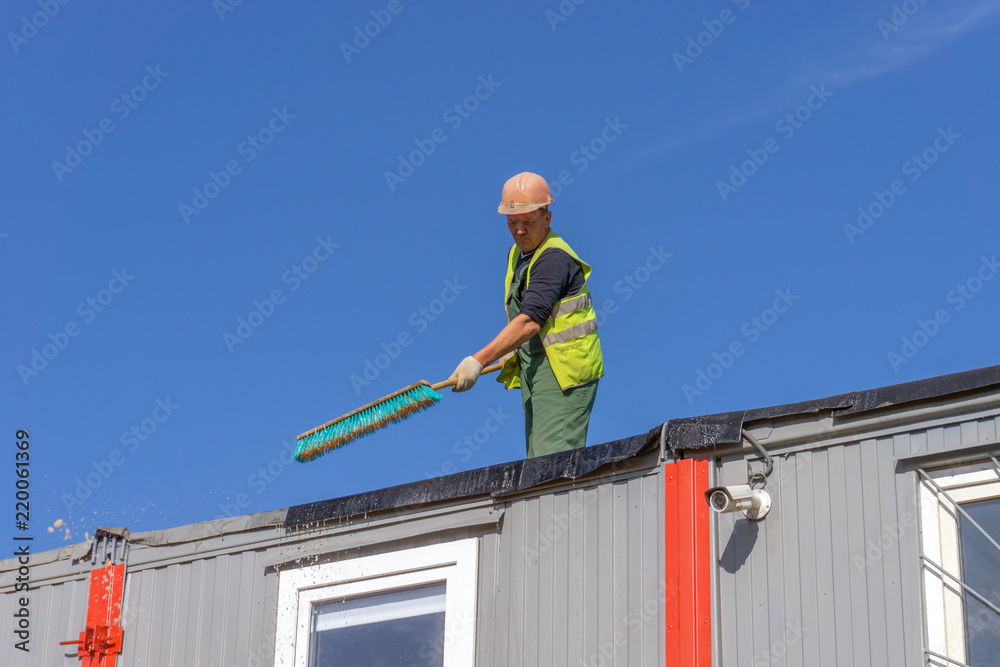 Worker at the construction site cleans the roof of the water with a brush