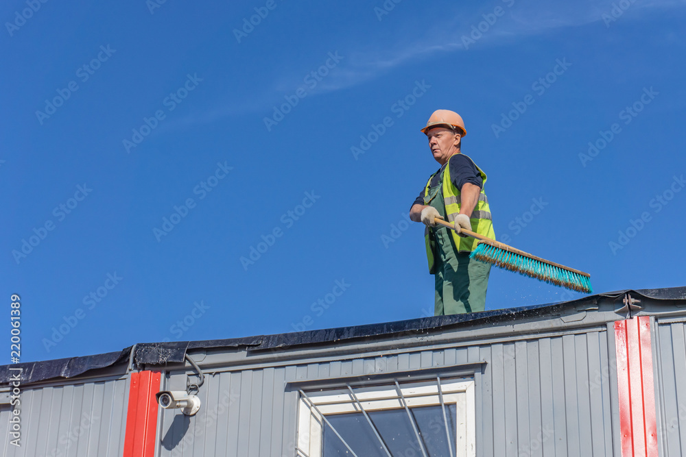 Worker at the construction site cleans the roof of the water with a brush