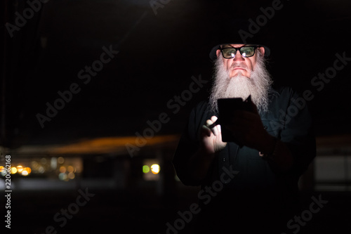 Mature bearded man using phone and looking suspicious