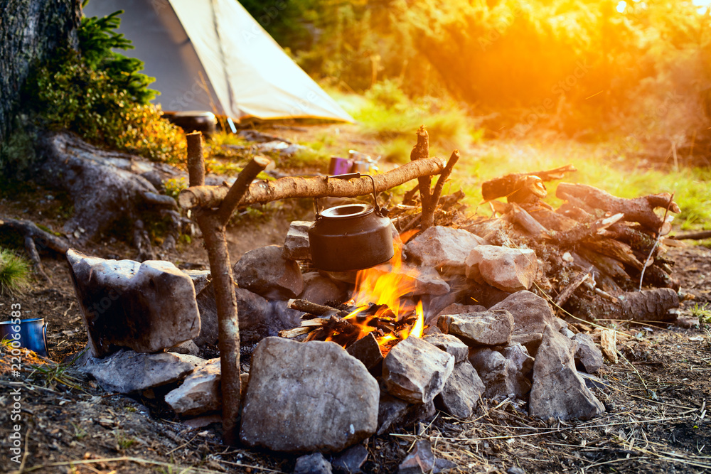 Old small kettle is heated on a bright bonfire - obrazy, fototapety, plakaty 