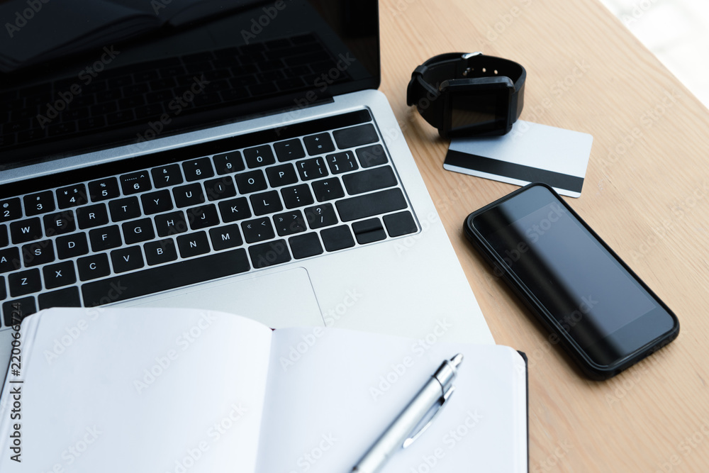 high angle view of laptop, smartwatch, smartphone, credit card and blank notebook with pen on table high angle view of laptop, smartwatch, smartphone, credit card and blank notebook with pen on table