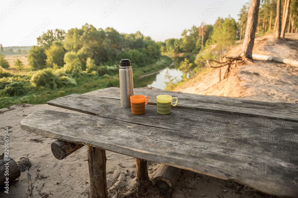 Coffee-drinking on the wild river bank during the hike. Cups with coffee and thermos on a wooden coarse table on the high bank of the river.
Coffee-drinking on the wild river bank during the hike. Cups with coffee and thermos on a wooden coarse table on the high bank of the river.