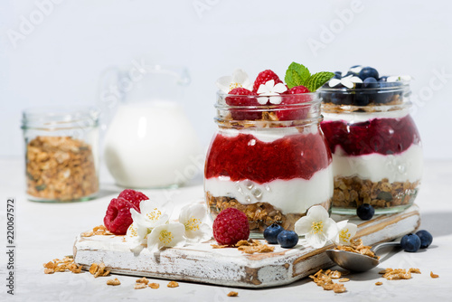 desserts with granola, berry and fruit puree in jars on white table, closeup