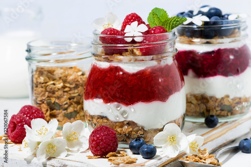 desserts with muesli, berry and fruit puree in jars on white table, closeup