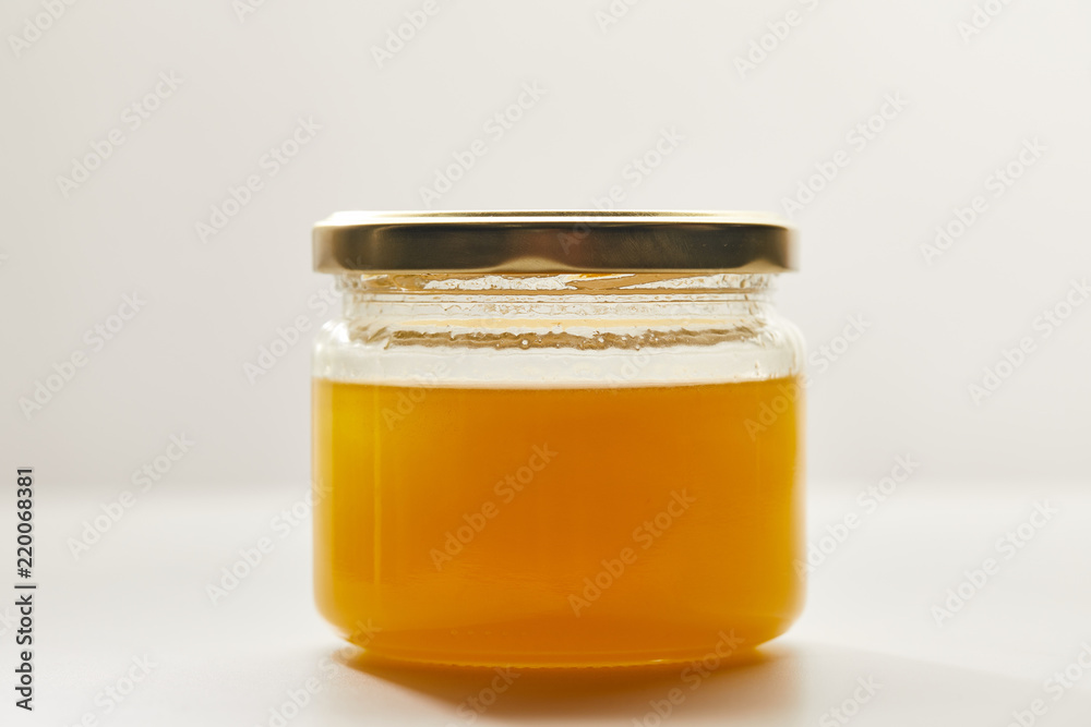 close up view of sweet organic honey in glass jar on white surface