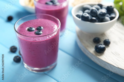 Glass with tasty blueberry smoothie on color wooden table