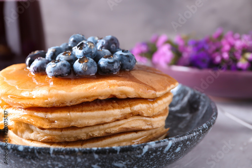 Bowl with tasty pancakes and blueberries on light table, closeup