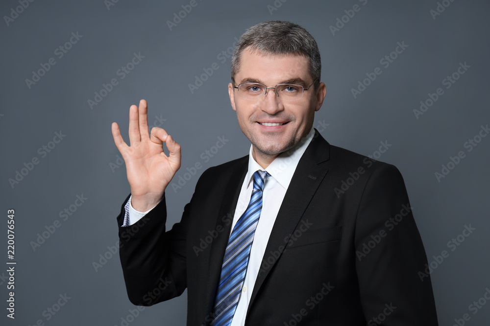 Handsome businessman showing OK gesture on grey background Handsome businessman showing OK gesture on grey background