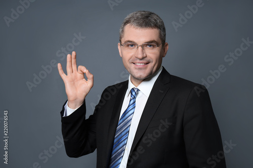 Handsome businessman showing OK gesture on grey background