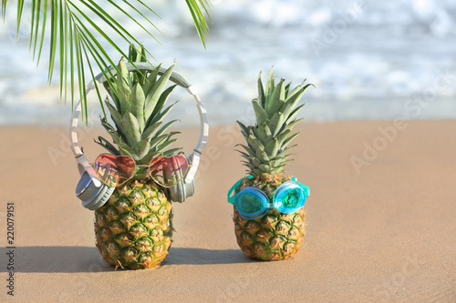 Funny pineapples with headphones and goggles on tropical beach