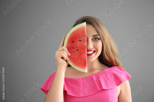 Beautiful young woman with slice of tasty watermelon on grey background