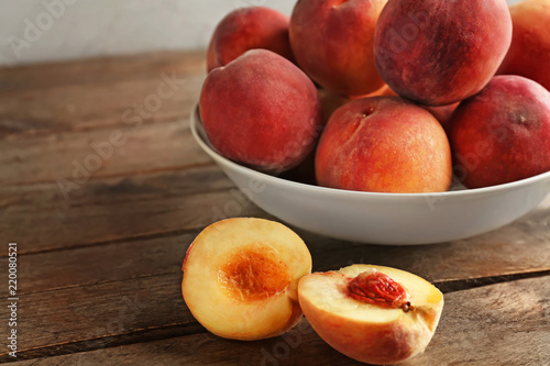 Bowl with fresh peaches on wooden table, closeup