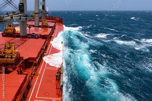Cargo ship rolling in stormy sea. Huge waves under blue sky in Indian Ocean