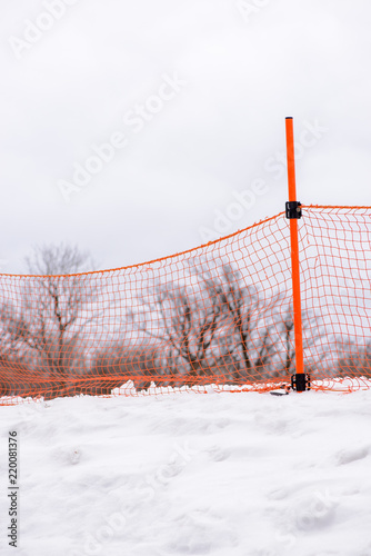 Wide close-up of orange net fences at the snowy ski slopes of the Gokase Highlands, cloudy day. Shallow focus vertical orientation. Miyazaki, Japan. Sports and seasons.