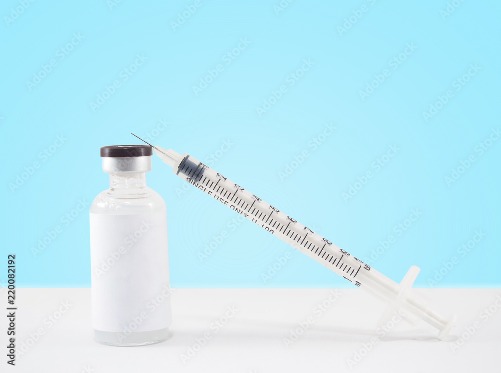 Blank label medical glass vial and plastic syringe for injection on white table with blue gradient background. Concept of vaccination, insulin and cosmetic injection. Copy space.
