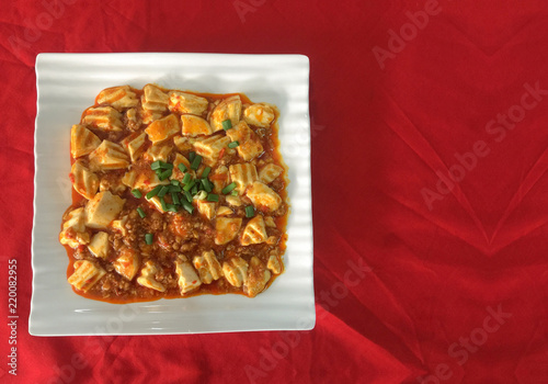chinese cuisine Mabo Tofu meal on white ceramic square dish with copy space red cloth table as background. photo