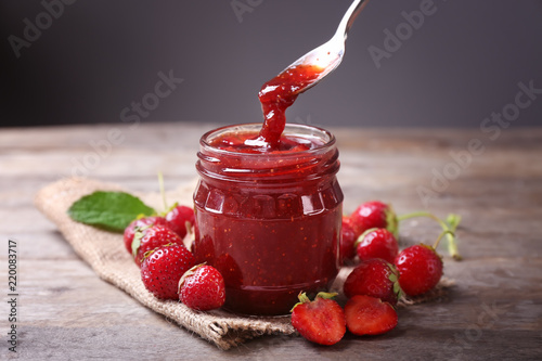 Glass jar and spoon with delicious strawberry jam on wooden table