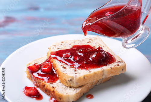 Pouring of delicious strawberry jam onto slices of bread, closeup