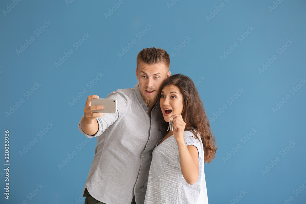 Happy young couple taking selfie with key from their new house on color background Happy young couple taking selfie with key from their new house on color background
